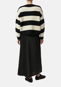 Person wearing a black and white striped sweater, long black skirt, and black sneakers, standing with back facing the viewer on white background.