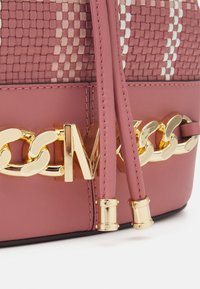 Sac à main tissé rose avec des accents en chaîne dorée et une base en cuir lisse. Longues poignées en cuir avec des détails en métal.