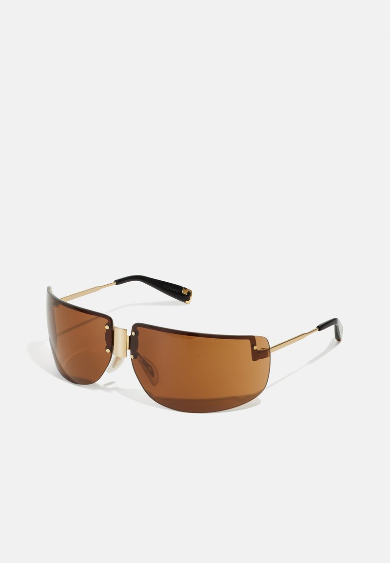 Lunettes de soleil teintées marron avec une forme courbée, des détails en or et des branches accentuées de noir. Texture lisse avec des détails de design minimalistes.