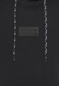 Black hooded sweatshirt featuring a textured black logo patch and contrasting black-and-white drawstrings. Smooth fabric with a fitted design.