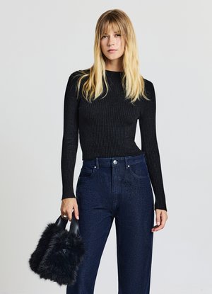 Schwarzes, geripptes Langarmshirt kombiniert mit dunkelblauen, hoch taillierten Jeans mit Nietenakzenten. Das Model hält eine schwarze Handtasche aus Kunstfell.