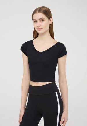 T-shirt nera a maniche corte, cropped, in tessuto a costine con scollatura a V, abbinata a leggings neri a vita alta con righe bianche ai lati.