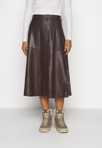 Bruine leren midi-rok met naaddetails, gecombineerd met tan hoge laarzen met veters en bontaccenten. Minimalistisch ontwerp, gladde textuur.