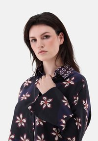 Dark floral shirt with bell sleeves, featuring a pattern of white and maroon flowers. Smooth fabric and a contrasting patterned collar.