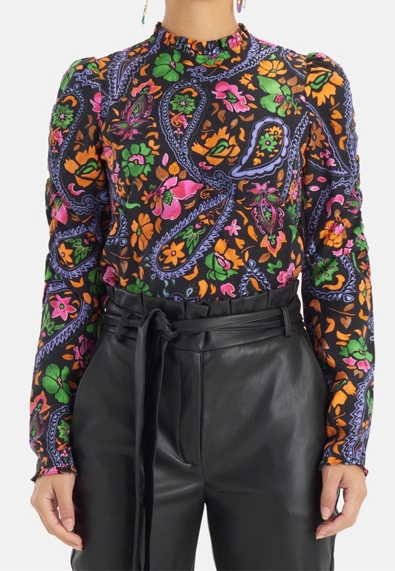 Blouse noire à manches longues avec imprimé floral coloré paisley, associée à un pantalon en cuir noir taille haute noué à la taille.
