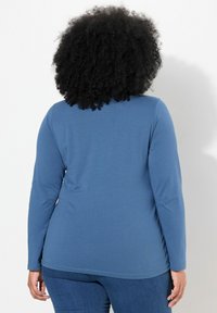 Halenka s dlouhým rukávem v modré látce, s hladkou texturou a kulatým výstřihem, ve spojení s přiléhavými džíny.