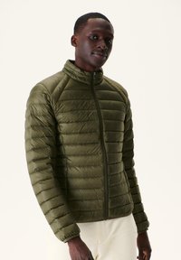 Chaqueta acolchada verde oliva con cuello alto, cierre de cremallera y costuras horizontales. Presenta un diseño ligero y acolchado.