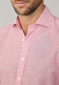 Red and white striped button-up shirt with a pointed collar and embroidered accent. Light fabric with a textured finish.