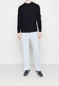 Granatowy sweter z ribbowanym splotem, z długim rękawem, w zestawieniu z jasnoniebieskimi dżinsami i ciemnymi butami sportowymi z białymi akcentami. Prosty design, bez wzorów.