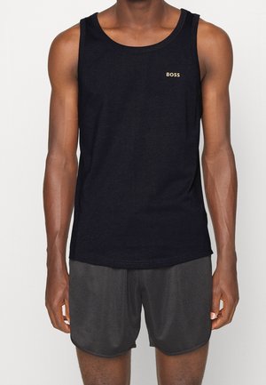 Mand iført en sort ærmeløs tanktop med "BOSS" logo og mørke teksturerede atletikshorts, stående mod en ensfarvet baggrund.