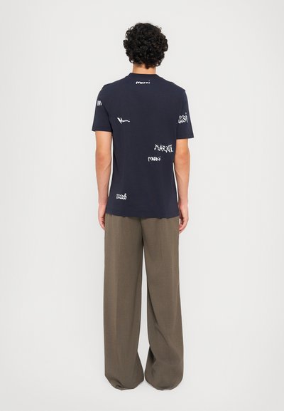 Marineblå bomulds T-shirt med afslappet pasform, med hvide "Marni" logo tryk spredt over ryggen. Bukserne er løstsiddende og grå.