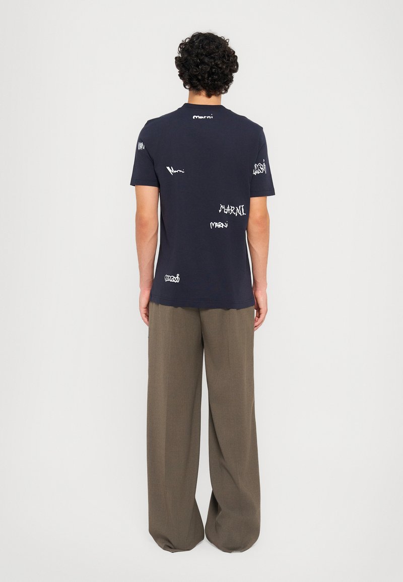 Camiseta de algodón azul marino con un corte relajado, que presenta estampados del logo blanco "Marni" dispersos por la parte posterior. Los pantalones son de corte holgado, grises.