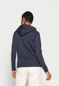 Sudadera azul marina hecha de una tela suave, con una gran capucha, mangas largas y puños acanalados. Textura lisa con un diseño minimalista.