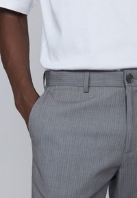 Pantalones rectos de rayas gris con corte recto, que cuentan con una cintura, bolsillos laterales y un cierre de botón. La tela parece suave con una textura sutil.