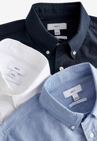 Tres camisas de botones en navy, blanco y azul claro. Hechas de algodón, con cuellos, botones y etiquetas de marca en el interior.