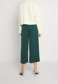 Cropped yellow sweatshirt with long sleeves, paired with green wide-leg trousers. Model wearing light-colored heeled sandals.