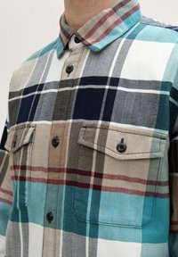 Kariertes Flanellhemd in Türkis, Marineblau, Beige und Burgunderrot. Mit einem Button-Down-Kragen und zwei Brusttaschen mit Klappenverschluss.