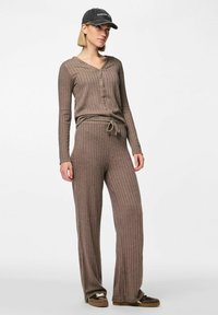 Brunt ribbat loungemodell som består av en långärmad skjorta med knappar och byxor med dragsko, tillverkad av ett mjukt, stretchigt material.