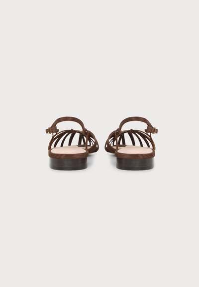 Paire de sandales plates marron avec des brides ouvertes et des boucles à la cheville, vue de dos sur fond blanc.