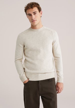 Suéter de punto beige con cuello redondo y puños y dobladillo acanalados. Combinado con pantalones oscuros, con un acabado texturizado.