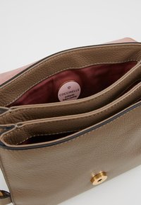 Interior de bolso de cuero marrón con forro rosa, que cuenta con dos compartimentos y una etiqueta de logo circular que muestra "Cuero italiano auténtico."