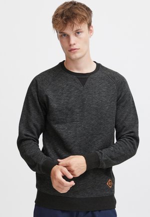 Sudadera de mélange negra con mangas raglán, cuello redondo, puños y dobladillo de canalé. Presenta un pequeño parche de logo marrón en la cintura.