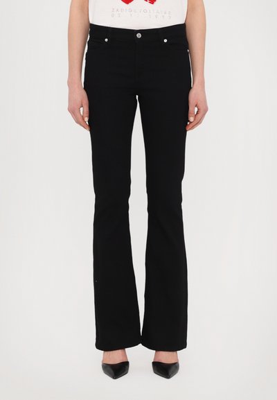 Jean noirs évasés avec une texture lisse, cinq poches et des éléments en métal argenté. Porté avec un T-shirt graphique blanc ajusté et des escarpins noirs pointus.
