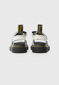 Svarte og hvite sandaler med åpen bakdesign, med en teksturert svart såle, gule detaljer og svarte hæl-trekk.