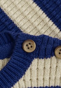 Strickstoff mit beigen und blauen Streifen, mit einer Nahaufnahme von zwei braunen Vierlochknöpfen an einem blauen Rippenrand.