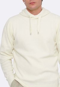 Felpa bianca realizzata in tessuto morbido, dotata di tasca a marsupio, cappuccio con lacci e punte in metallo, e polsini e orlo a costine.