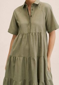 Khakigrünes, schichtweise gestaltetes Kleid mit kurzen Ärmeln, Kragen und Knopfdetails, gefertigt aus weichem, strukturiertem Stoff.