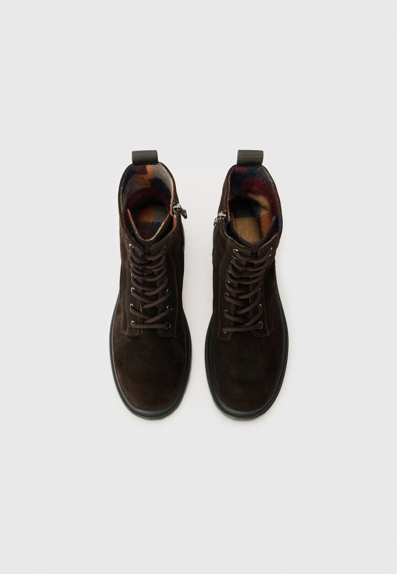 Braune Wildleder-Stiefeletten mit Schnürsenkeln, strukturiertem Obermaterial und buntem Karolining. Mit Zugschlaufe und seitlichem Reißverschluss. Gummisohle.