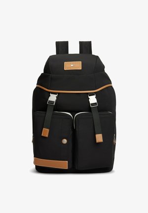 Zaino nero con due tasche frontali con zip, rifiniture in pelle marrone, spallacci regolabili e una toppa rettangolare con logo al centro in alto.