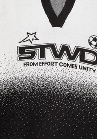 Maillot de sport noir et blanc à col en V, avec un motif de points en dégradé, le texte "STWD" et un graphique de ballon de football. Texture de tissu doux.