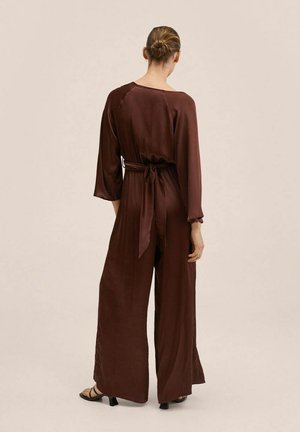 Brauner Satin-Jumpsuit mit langen Ärmeln, tailliertem Gürtel, weiter Beinführung und glatter Textur. Rückansicht betont minimalistisches Design.