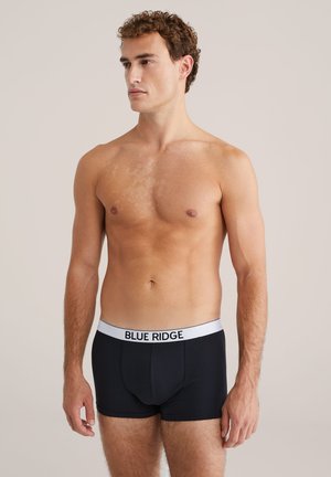 Boxer shorts neri in cotone, con una cintura bianca su cui è stampato "BLUE RIDGE". Il modello è in piedi, con il torso visibile.