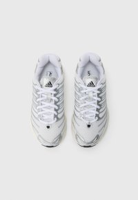 Fehér futócipő hálós felsőrésszel, ezüst díszítésekkel és fényvisszaverő részletekkel. Fűzőzáras és texturált talpú a jobb tapadás érdekében.