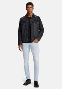 Czarna dżinsowa kurtka z dwoma kieszeniami na piersi, zestawiona z czarnym t-shirtem i jasnoniebieskimi dżinsami slim fit. Całość dopełniają czarne buty.