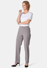 Hellgraue Hose mit schmaler Passform, ausgestattet mit einem eleganten Bund und einem dezenten Bügeln. Kombiniert mit einem weißen kurzärmeligen Oberteil und schwarzen High Heels.