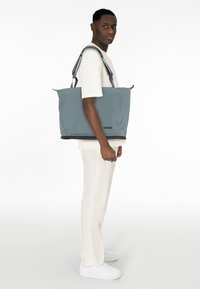 Sac fourre-tout Thule gris avec deux poignées, un extérieur lisse et une base noire, présentant un design simple et un minimum de branding.
