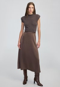 Brązowa dopasowana wełniana bluzka z rękawami typu cap, w zestawie z długą brązową satynową spódnicą z bocznym rozcięciem i paskiem do związania, uzupełniona wysokimi brązowymi butami do kolan.