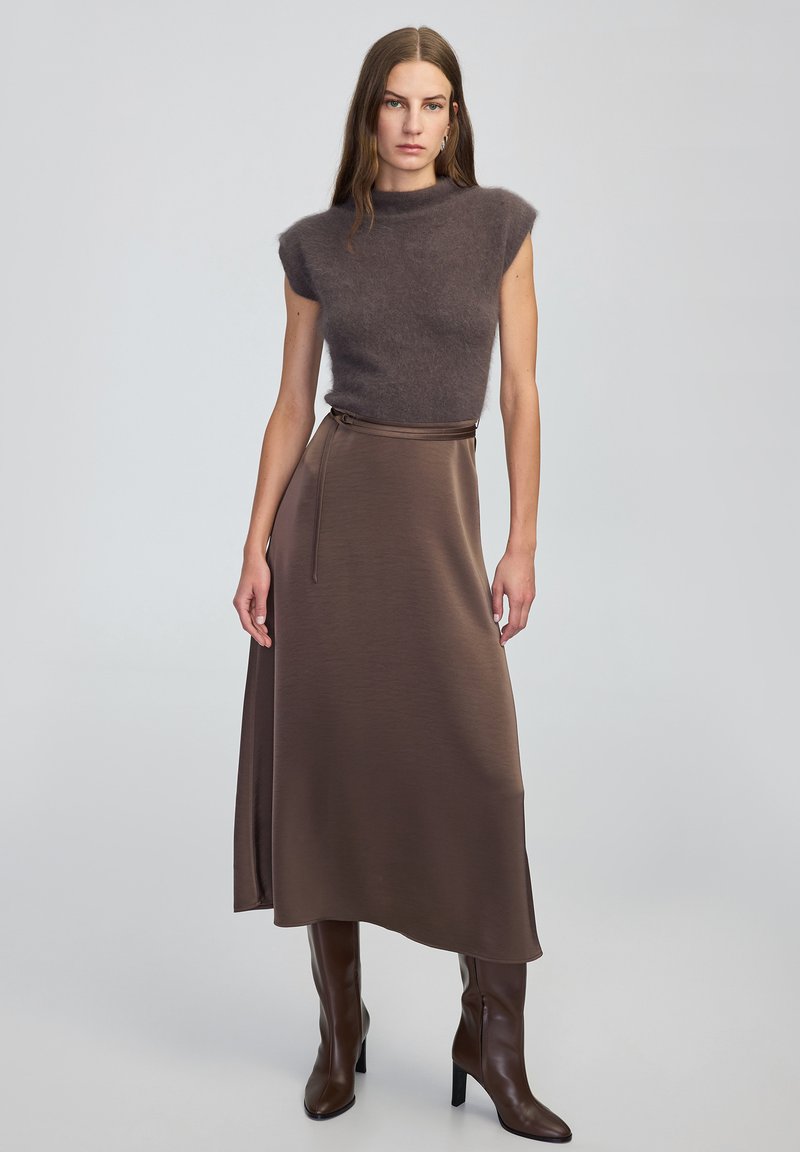 Brązowa dopasowana wełniana bluzka z rękawami typu cap, w zestawie z długą brązową satynową spódnicą z bocznym rozcięciem i paskiem do związania, uzupełniona wysokimi brązowymi butami do kolan.