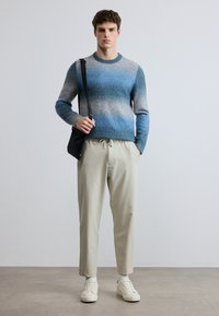 Sininen ja harmaa ombre-neulepaita, beiget nyörivahteiset housut, valkoiset tennarit. Malli pitää mustaa laukkua. Sileät tekstuurit, rento istuvuus, moderni muotoilu.