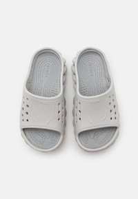 Grå, lätta slip-on sandaler med en texturerad fotbädd, perforerat ovandel för ventilation och en vågig sula. Varumärkesnamnet synligt.