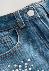 Jeans i denim med en ljusblå tvätt, synliga sömmar och dekorativa rhinestones arrangerade i ett mönster på framsidan.