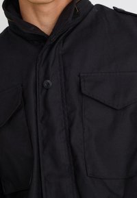 Czarna kurtka z wysokim kołnierzem, dwoma kieszeniami na piersiach, zapięciem na guziki oraz teksturowanym materiałem. Design wyróżnia się czystą, smukłą sylwetką.