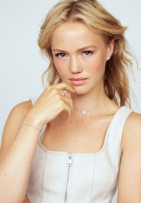 Smycken med silverfärgad fjärilstema, inklusive örhängen, halsband och armband, uppvisade med en ljusgrå, ärmlös topp.