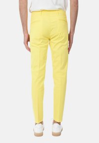 Pantaloni gialli sartoriali, slim fit, con una texture liscia e tasche posteriori. Indossati con sneaker bianche con suole in gomma.