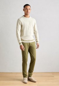Lysfarget strikket genser med ribbestrikket hals og mansjetter, sammen med olivengrønne slim-fit bukser og beige slips-on sko.