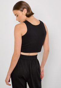 Schwarzes, kurz geschnittenes Tanktop mit rundem Ausschnitt und gerippter Textur, kombiniert mit locker sitzenden schwarzen Hosen mit elastischem Bund.